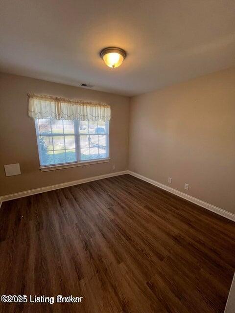 unfurnished room featuring dark wood-style floors, visible vents, and baseboards