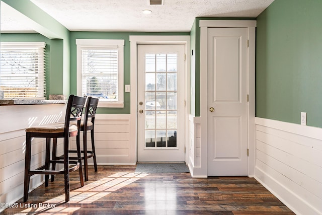 doorway to outside featuring dark wood finished floors, wainscoting, a textured ceiling, and wood walls