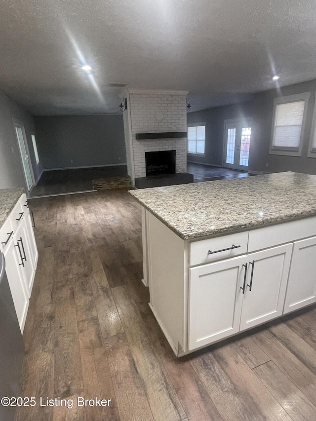 kitchen with dark wood-type flooring, light stone counters, a textured ceiling, white cabinets, and a brick fireplace