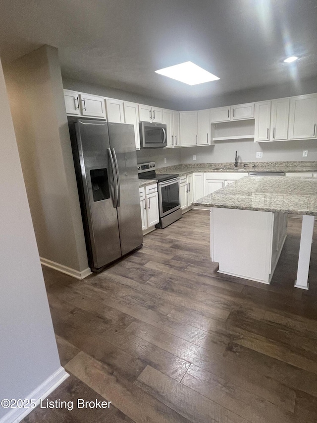 kitchen with light stone countertops, dark wood-style flooring, a sink, white cabinets, and appliances with stainless steel finishes