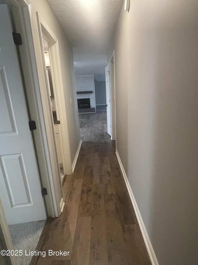 corridor with a textured ceiling, baseboards, and dark wood-style flooring