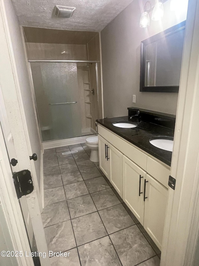 bathroom featuring visible vents, double vanity, a sink, a shower stall, and a textured ceiling