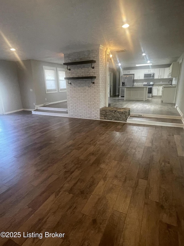 unfurnished living room featuring dark wood finished floors, a sink, baseboards, and a textured ceiling