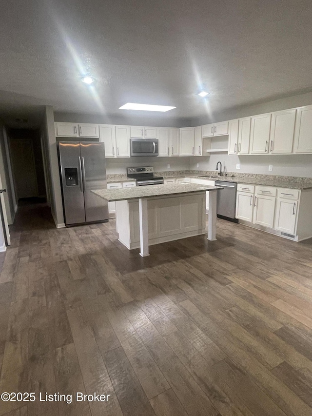 kitchen with dark wood-style floors, a kitchen island, white cabinets, and stainless steel appliances