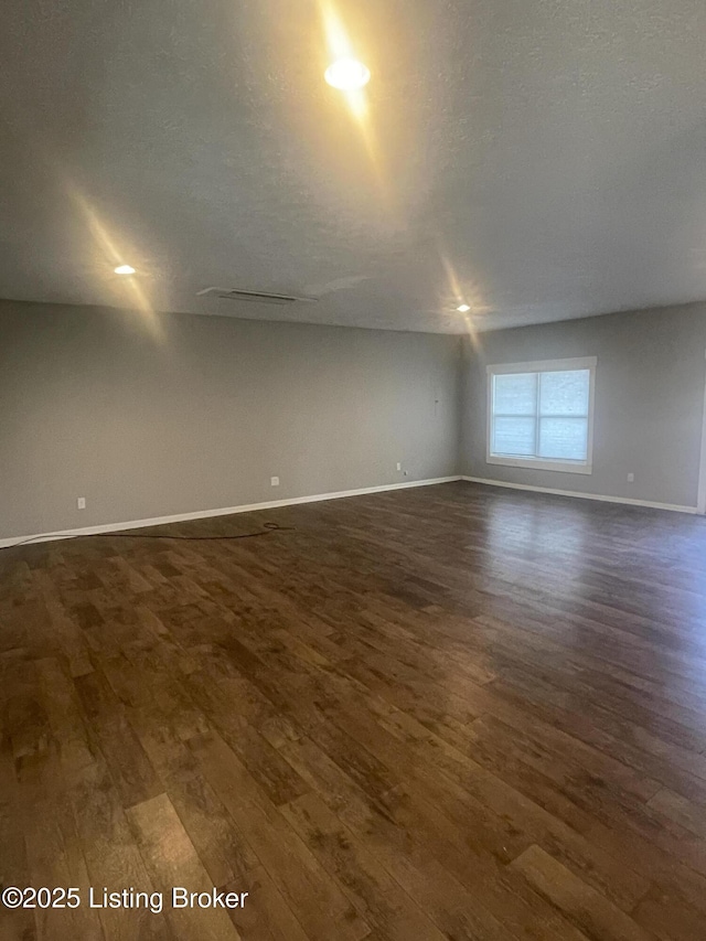 empty room featuring dark wood-type flooring, baseboards, and a textured ceiling