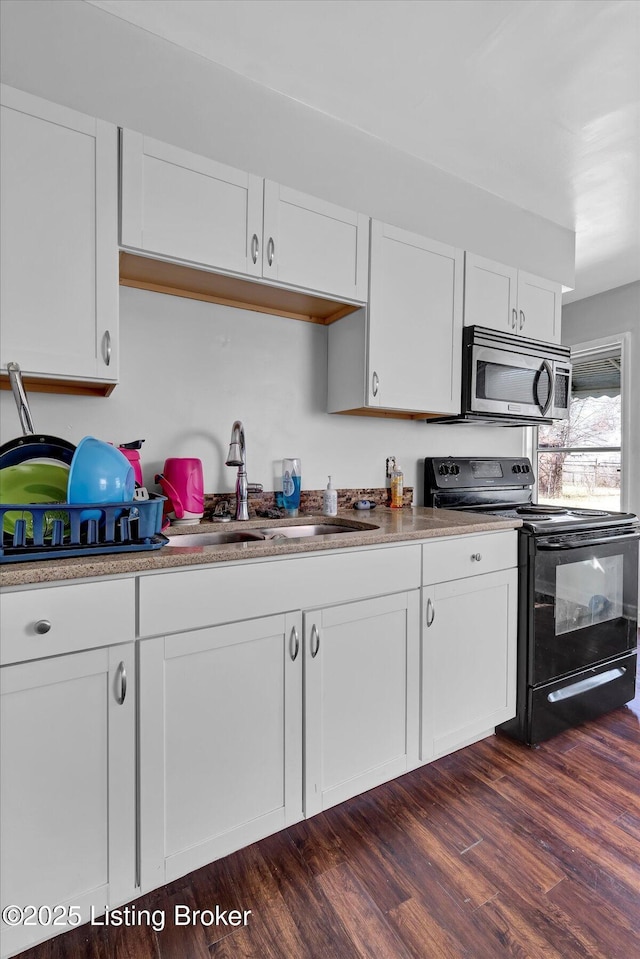 kitchen featuring electric range, a sink, dark wood-type flooring, white cabinetry, and stainless steel microwave