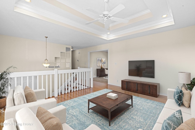 living area featuring baseboards, ornamental molding, wood finished floors, a raised ceiling, and a ceiling fan