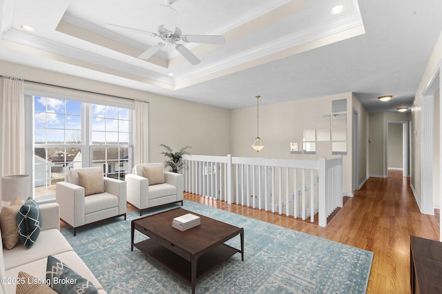 living room with baseboards, a raised ceiling, wood finished floors, and ornamental molding