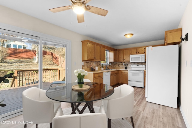 kitchen featuring backsplash, light countertops, light wood-style flooring, white appliances, and a sink