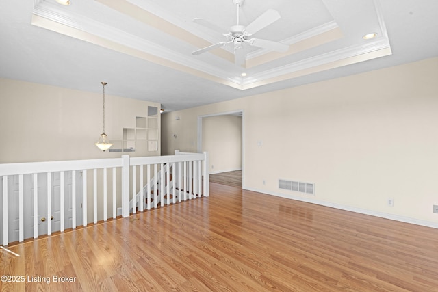 unfurnished room with baseboards, visible vents, a tray ceiling, ornamental molding, and light wood-type flooring