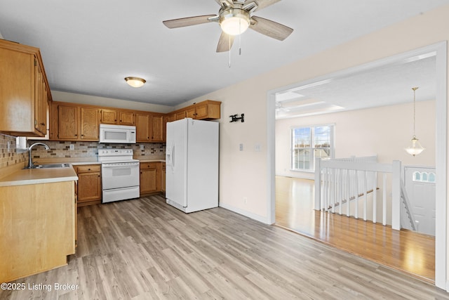 kitchen with backsplash, light countertops, light wood-style floors, white appliances, and a sink