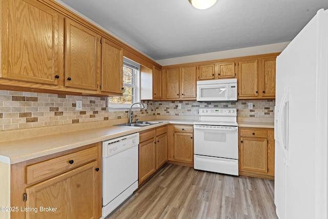 kitchen with white appliances, light wood finished floors, a sink, decorative backsplash, and light countertops