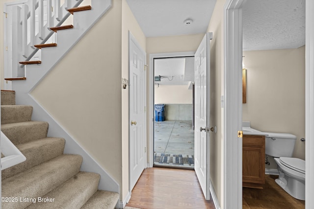 staircase with wood finished floors, baseboards, and a textured ceiling