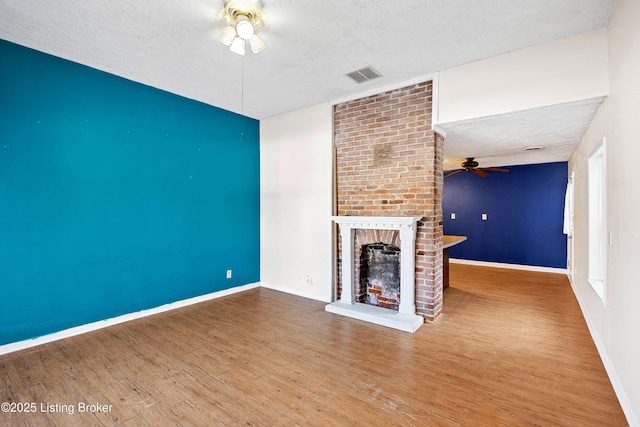 unfurnished living room with a textured ceiling, wood finished floors, visible vents, and ceiling fan