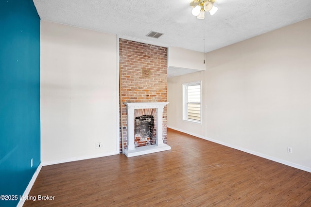 unfurnished living room with visible vents, a fireplace, wood finished floors, a textured ceiling, and a ceiling fan