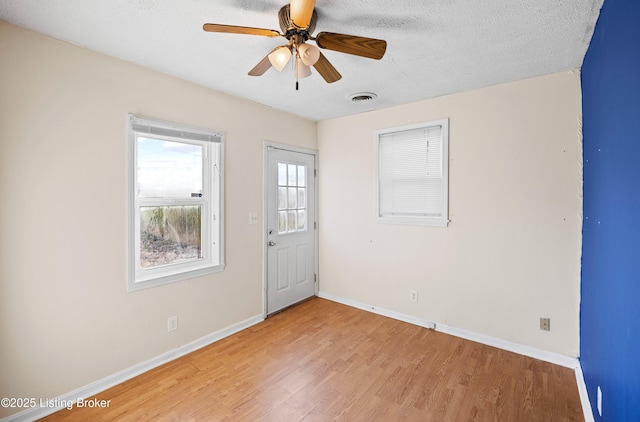 unfurnished room with light wood finished floors, visible vents, baseboards, a textured ceiling, and a ceiling fan