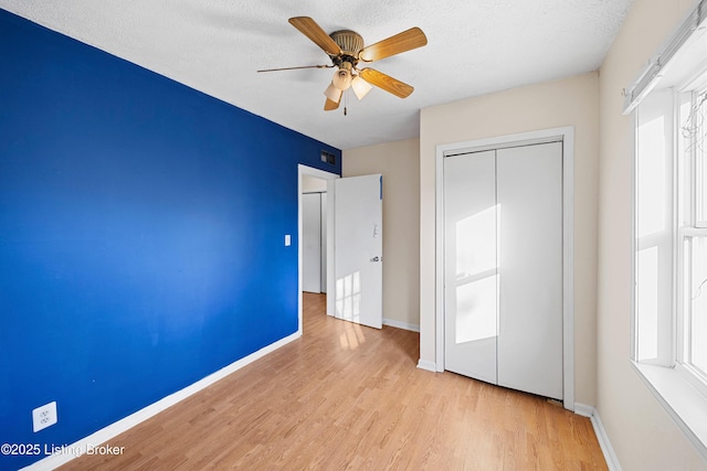 unfurnished bedroom featuring multiple windows, light wood-style floors, a closet, and baseboards