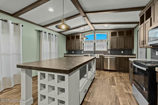 kitchen with lofted ceiling with beams, a sink, light wood-style floors, appliances with stainless steel finishes, and dark countertops