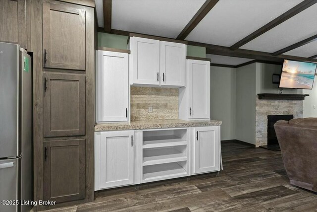 kitchen with backsplash, white cabinetry, freestanding refrigerator, a stone fireplace, and dark wood-style flooring