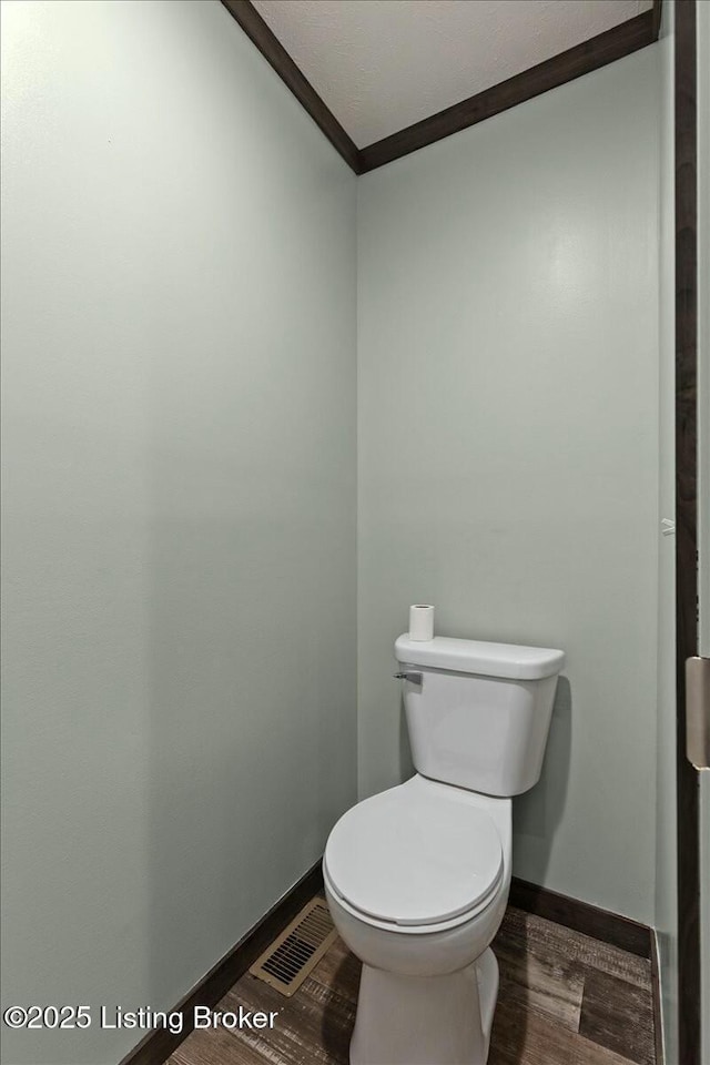 bathroom with toilet, wood finished floors, visible vents, and ornamental molding