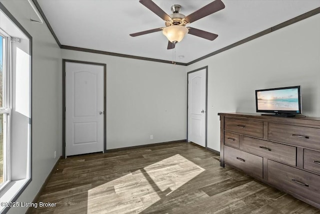 unfurnished bedroom with crown molding, a ceiling fan, dark wood-style flooring, and baseboards