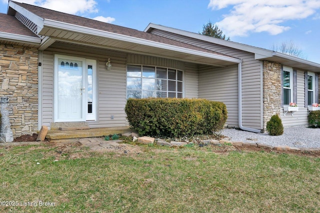 doorway to property with a yard, stone siding, and a shingled roof