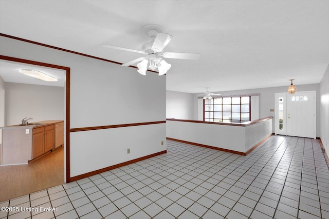 spare room with light tile patterned floors, ceiling fan, baseboards, and a sink