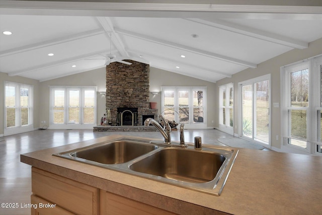 kitchen featuring a sink, lofted ceiling with beams, open floor plan, a fireplace, and ceiling fan