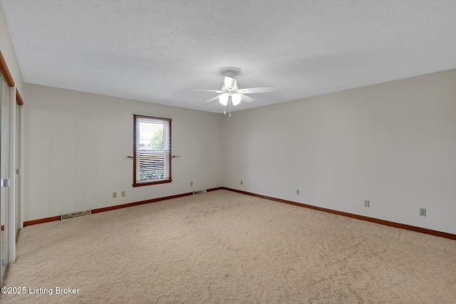 carpeted empty room with visible vents, ceiling fan, a textured ceiling, and baseboards