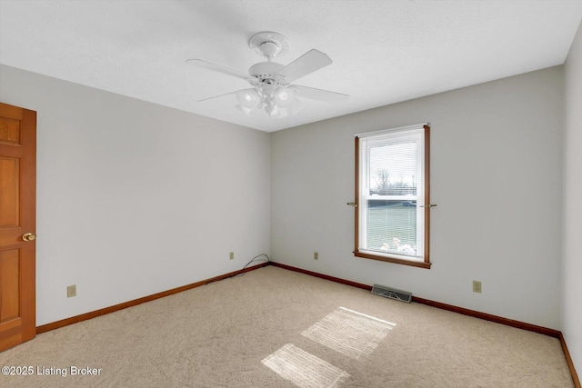 spare room featuring a ceiling fan, light colored carpet, visible vents, and baseboards