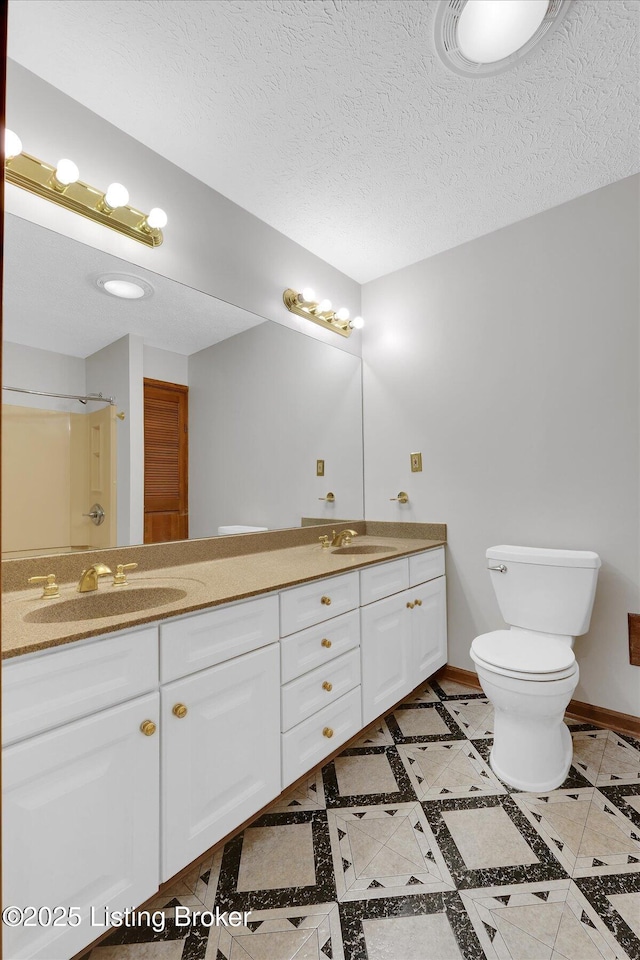 bathroom with a textured ceiling, double vanity, baseboards, and a sink