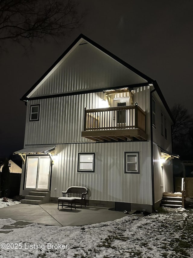 back of house at night featuring entry steps, a patio, and a balcony