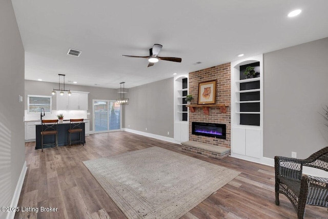 living room with visible vents, a fireplace, built in shelves, and wood finished floors