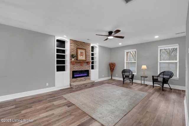 living area featuring wood finished floors, baseboards, a brick fireplace, and built in shelves