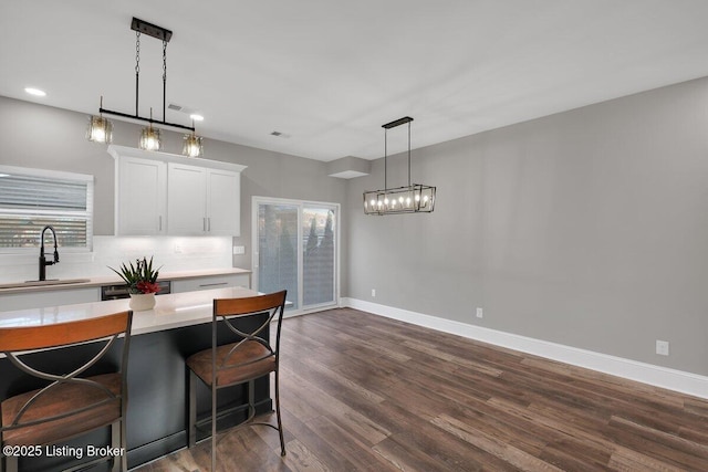 kitchen with tasteful backsplash, a sink, baseboards, white cabinetry, and dark wood-style flooring