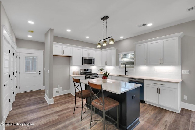 kitchen featuring wood finished floors, visible vents, a sink, appliances with stainless steel finishes, and white cabinetry