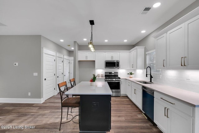 kitchen featuring dark wood-style floors, a kitchen island, a sink, appliances with stainless steel finishes, and white cabinetry