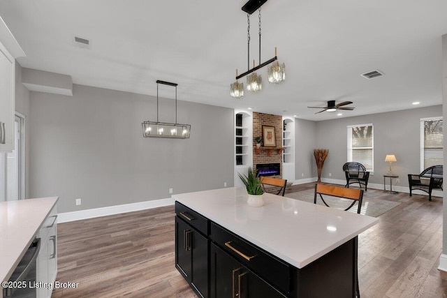 kitchen featuring light wood-type flooring, visible vents, dark cabinetry, light countertops, and a brick fireplace