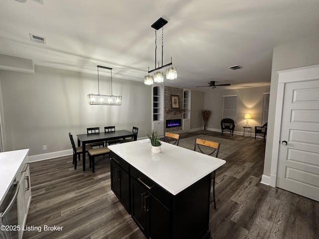 kitchen with visible vents, a brick fireplace, dark cabinetry, and dark wood-style flooring