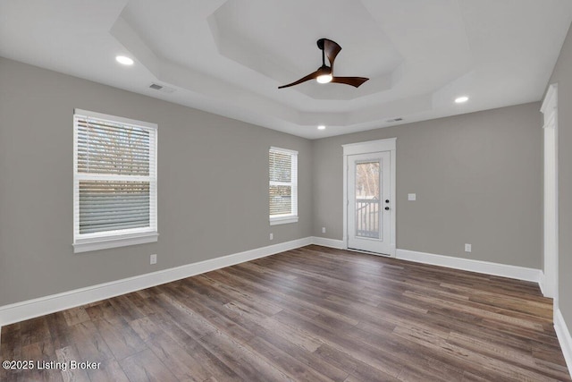 empty room featuring a tray ceiling, baseboards, dark wood-type flooring, and visible vents