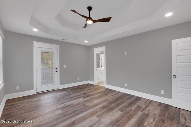 empty room with a tray ceiling, baseboards, wood finished floors, and a ceiling fan