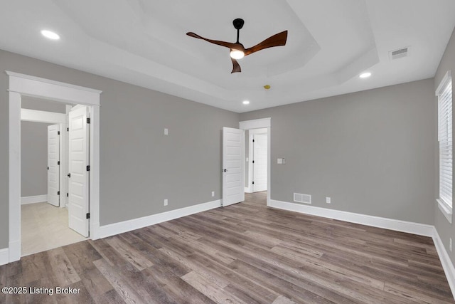 empty room featuring a tray ceiling, wood finished floors, visible vents, and baseboards