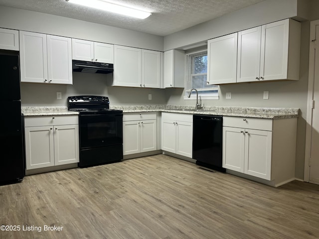 kitchen with black appliances, light wood-style floors, under cabinet range hood, a textured ceiling, and white cabinetry