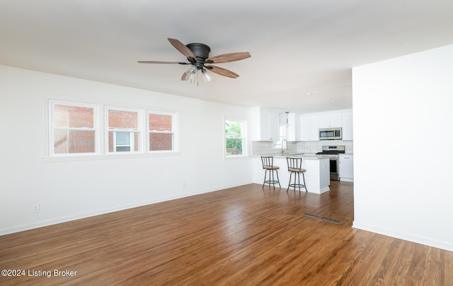 unfurnished living room with a ceiling fan, wood finished floors, baseboards, and a sink