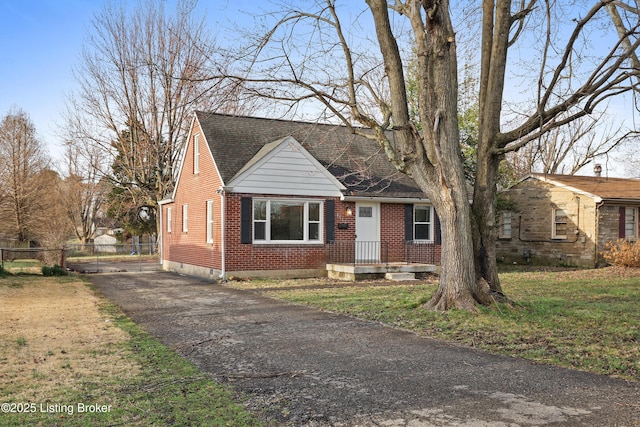 cape cod house with fence, brick siding, driveway, and a shingled roof