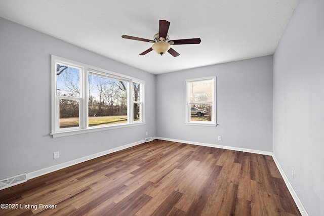 empty room featuring a wealth of natural light, visible vents, baseboards, and wood finished floors