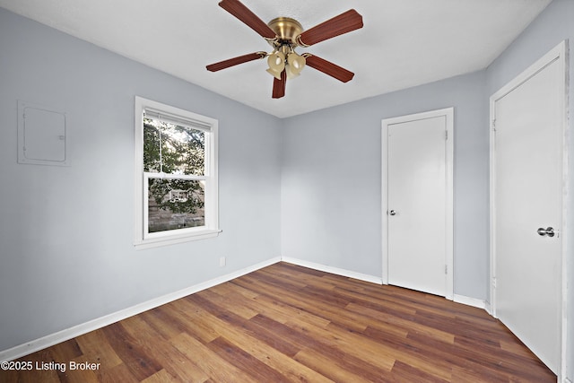 spare room featuring electric panel, baseboards, ceiling fan, and wood finished floors