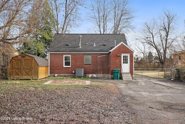 back of property with a storage unit, brick siding, roof with shingles, and entry steps