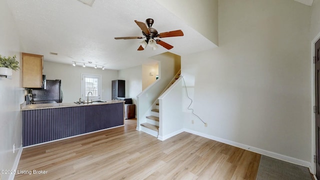 kitchen with baseboards, a peninsula, ceiling fan, a sink, and light wood-style floors