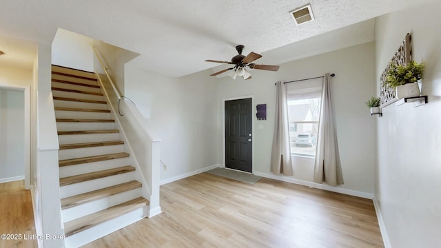 entryway featuring light wood-type flooring, visible vents, a textured ceiling, baseboards, and stairs